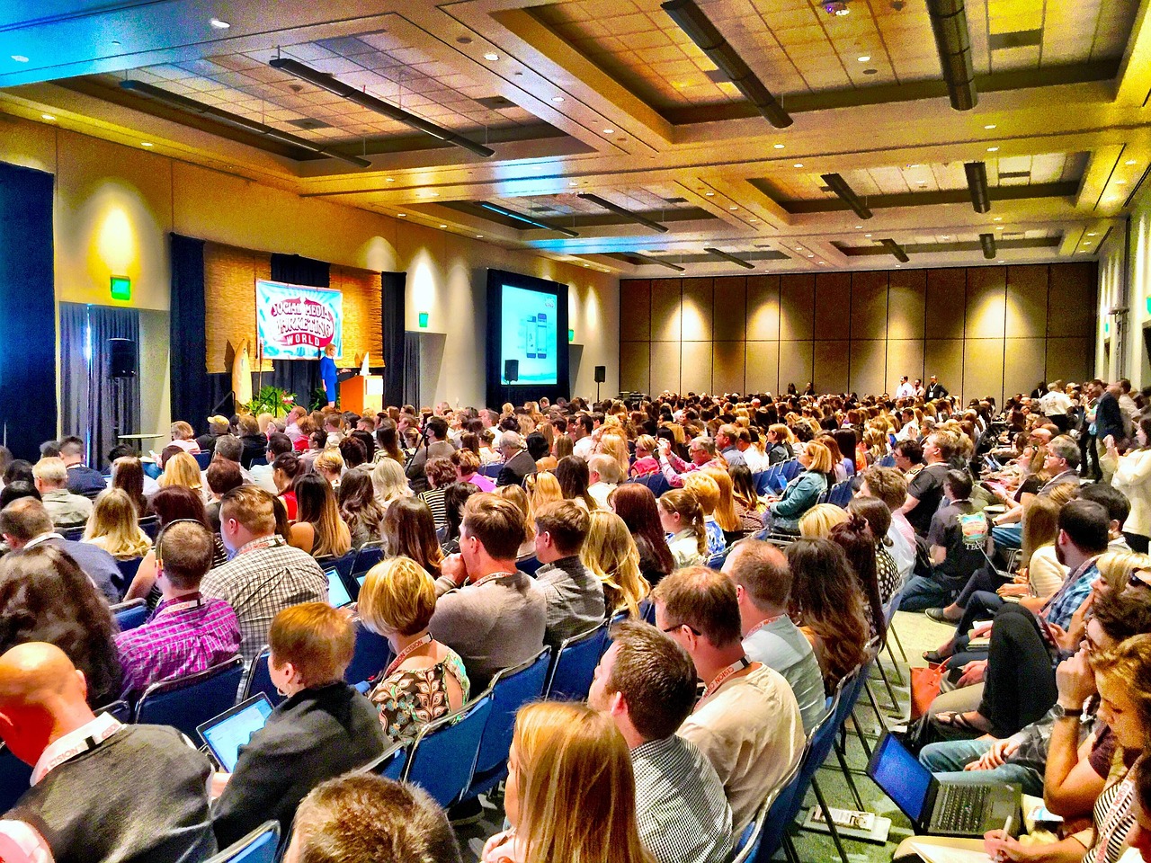 A full conference hall with people watching a speaker on stage